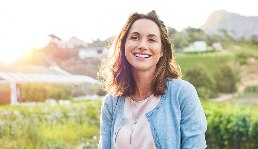 A woman standing outside, smiling while the sun sets.